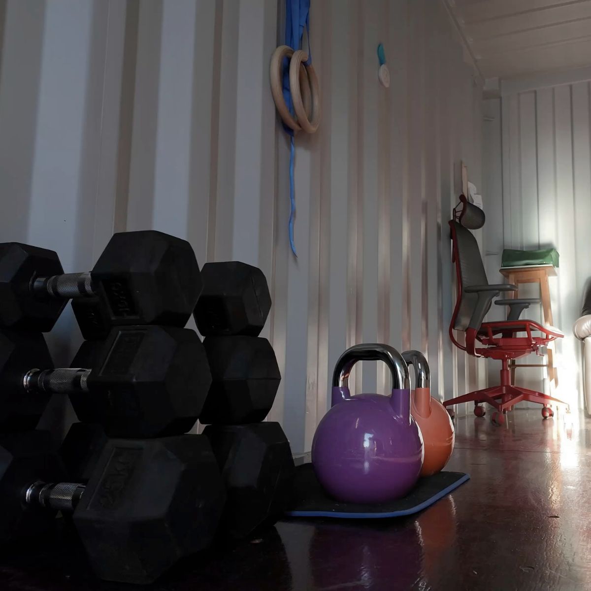 Trainingsbereich im Base33 Container Studio mit Kurzhanteln, Kettlebells und Turnringen